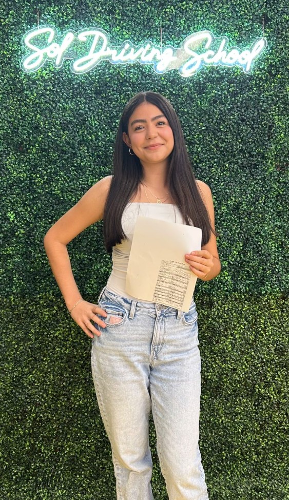 Student holding certificate in front of SOL Driving School sign